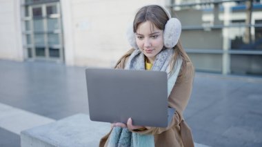 Young blonde woman using laptop sitting on bench at street