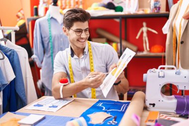 Young hispanic man tailor showing clothing design speaking at atelier