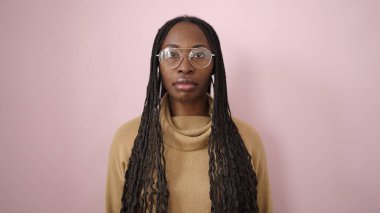 African woman standing with serious expression wearing glasses over isolated pink background