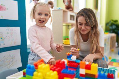 Teacher and toddler playing with construction blocks sitting on table at kindergarten