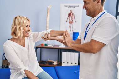 Orta yaşlı erkek ve kadın fizyoterapist ve kollarını esneten hasta fizik tedavi kliniğinde rehabilitasyon seansı yapıyorlar.