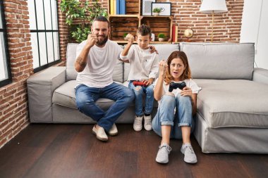 Üç kişilik aile kanepede oturup oyun oynuyor öfkeyle bağırıyor, öfkeyle bağırıyor ve el kaldırıyor. 