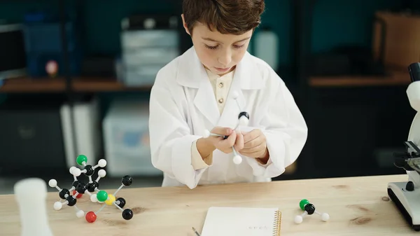 Adorable hispanic boy student holding molecules toy at laboratory classroom
