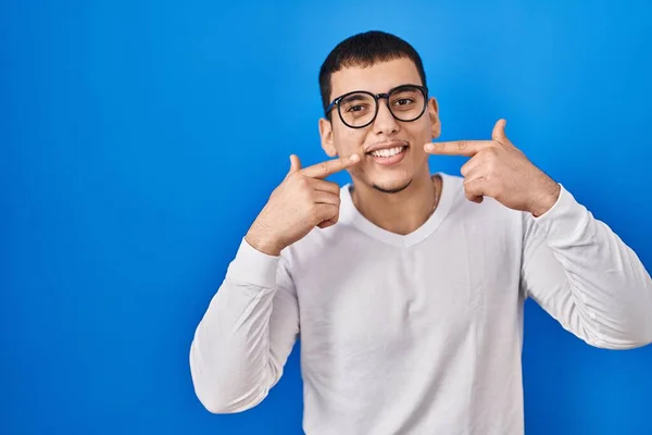 年轻的阿拉伯男子穿着随意的白色衬衫 戴着眼镜 笑容满面 用手指 牙齿和嘴指尖 牙齿健康概念 — 图库照片