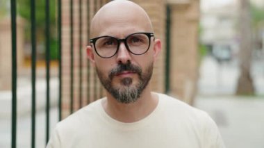 Genç kel adam gülümsüyor. Sokakta gözlük takıyor.