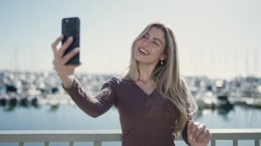 Genç sarışın kadın gülümsüyor. Sahilde kendine güvenen bir video görüşmesi var.