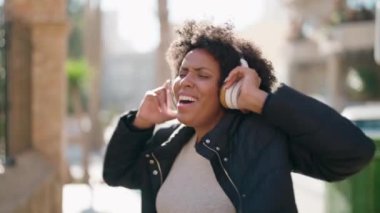 Genç Afro-Amerikalı kadın gülerek sokakta müzik dinliyor.
