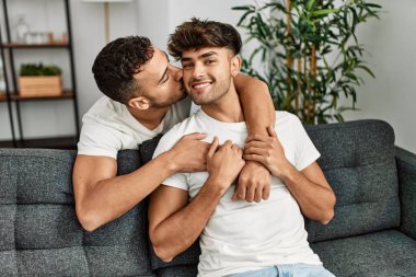 İki İspanyol erkek, kendilerine güvenerek gülümsüyor ve evde birbirlerine sarılıyorlar.