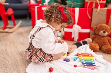 Adorable hispanic girl playing xylophone sitting on floor by christmas tree at home