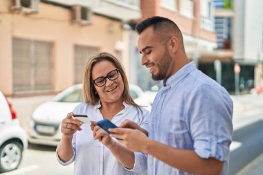 Man and woman mother and daugther using smartphone and credit card at street