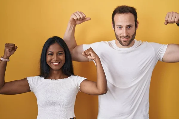 Interracial Couple Standing Yellow Background Showing Arms Muscles Smiling Proud — Stock Photo, Image