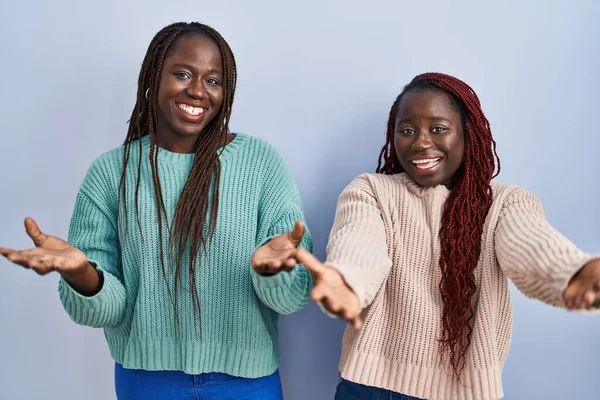 Две Африканки Стоящие Синем Фоне Весело Улыбаются Предлагая Руки Помогая — стоковое фото