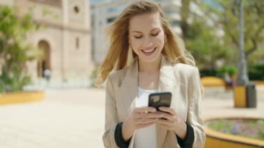 Parkta akıllı telefon kullanan, kendine güvenen genç sarışın kadın.