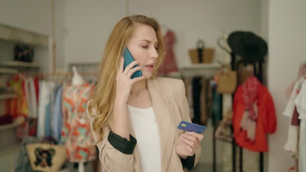 若いですブロンド女性顧客話して上のスマートフォン保持クレジットカードで服店 — ストック動画