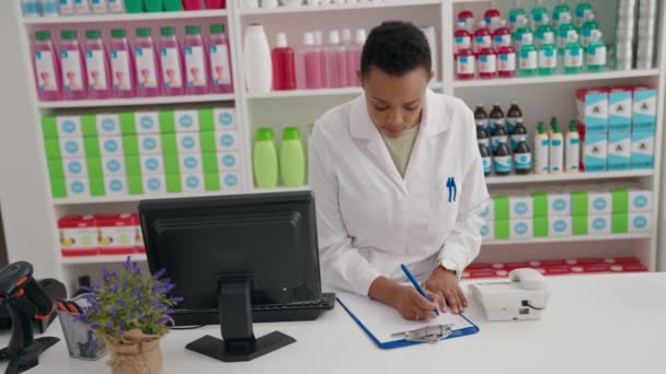 アフリカ系アメリカ人女性薬剤師が薬局でコンピュータを使って文書を書く — ストック動画