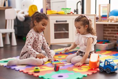 Two kids playing xylophone sitting on floor at kindergarten