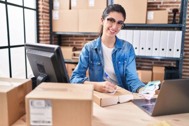 Genç ve güzel İspanyol kadın ecommerce iş işçisi. Ofisteki pakette akıllı telefon yazısını kullanıyor.