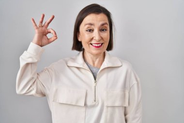 Orta yaşlı İspanyol kadın izole edilmiş arka planda durup gülümsüyor ve el ve parmaklarıyla 