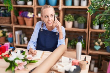 Çiçekçide, çiçekçi, çiçekçi defterine akıllı telefon yazısıyla konuşan genç sarışın kadın.