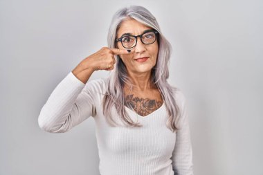 Middle age woman with grey hair standing over white background pointing with hand finger to face and nose, smiling cheerful. beauty concept 