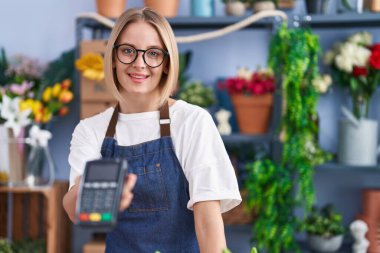 Young blonde woman florist smiling confident holding data phone at florist shop