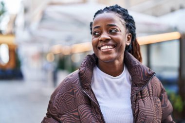 Afro-Amerikalı bir kadın kahvecinin terasında kendinden emin bir şekilde gülümsüyor.