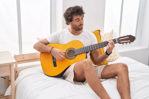 在卧室的床上弹奏古典吉他的年轻人 — 图库照片