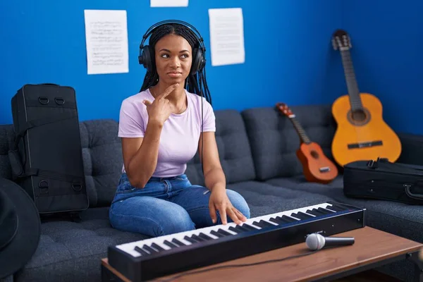 アフリカ系アメリカ人の女性がピアノのキーボードを弾いている音楽スタジオで深刻な顔はあごに手で質問について考えている 混乱のアイデアについて思慮深く — ストック写真
