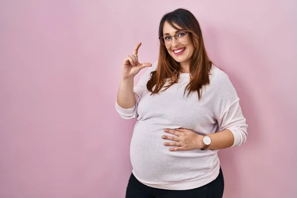 Těhotná Žena Stojí Nad Růžovým Pozadím Usmívá Sebevědomě Gestikuluje Rukou — Stock fotografie