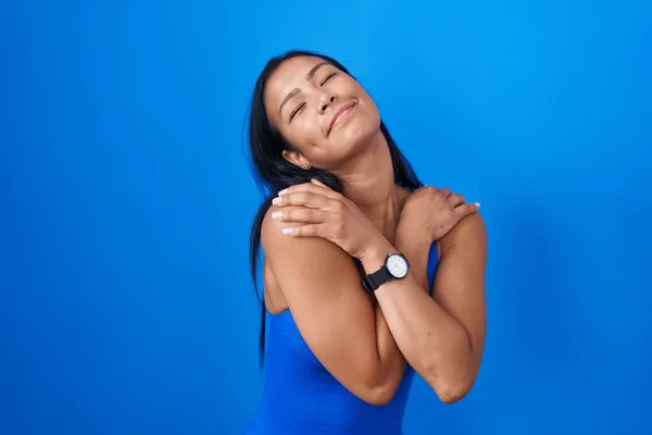 Hispanic Woman Standing Blue Background Hugging Oneself Happy Positive Smiling — Φωτογραφία Αρχείου