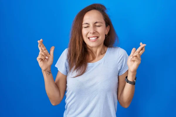 Brunette Woman Standing Blue Background Gesturing Finger Crossed Smiling Hope — Foto de Stock