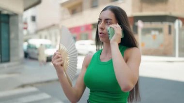 Genç, güzel, İspanyol bir kadın akıllı telefonla konuşuyor. Sokakta pervane kullanıyor.