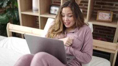Young beautiful hispanic woman having video call sitting on bed at bedroom