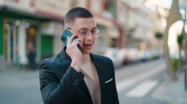 Genç İspanyol yönetici gülümseyerek caddede akıllı telefondan konuşuyor.