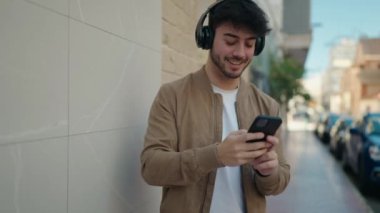 Young hispanic man smiling confident listening to music using smartphone at street