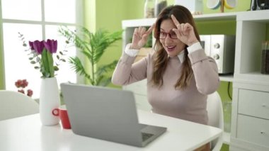 Genç, güzel, İspanyol bir kadın evdeki masada oturmuş video görüşmesi yapıyor.