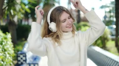 Young blonde woman listening to music and dancing at park