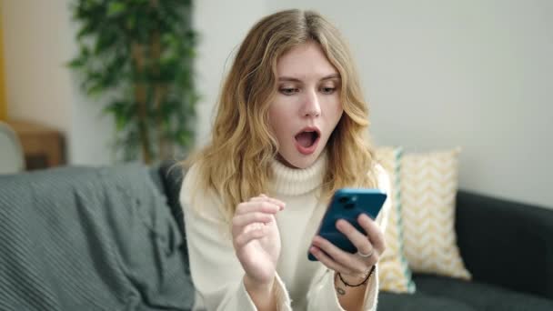 Junge Blonde Frau Nutzt Smartphone Mit Siegerausdruck Hause — Stockvideo