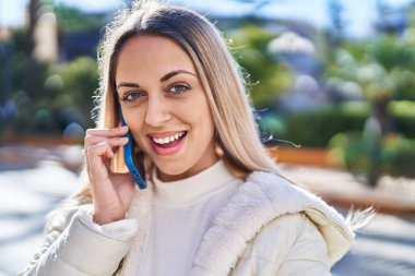 Gülümseyen genç bir kadın caddedeki akıllı telefondan konuşuyor.