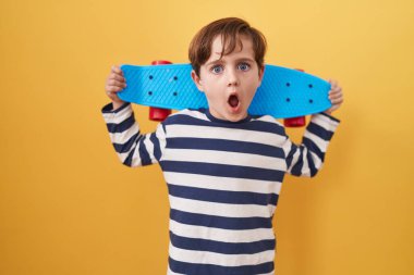 Sarı arka planda paten tutan küçük beyaz çocuk şaşkınlık ve şaşkınlık dolu bir ifade, korku ve heyecanlı bir yüz ifadesiyle şoka uğradı.. 