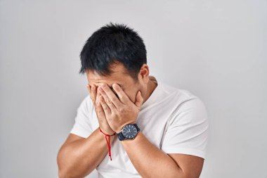 Young chinese man standing over white background with sad expression covering face with hands while crying. depression concept. 