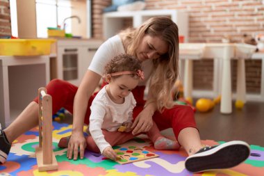 Teacher and toddler playing with maths puzzle game sitting on floor at kindergarten