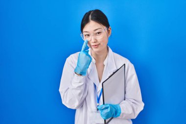 Chinese young woman working at scientist laboratory pointing to the eye watching you gesture, suspicious expression 