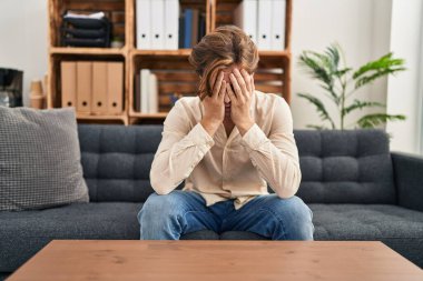 Young caucasian man patient stressed sitting on sofa at psychology clinic