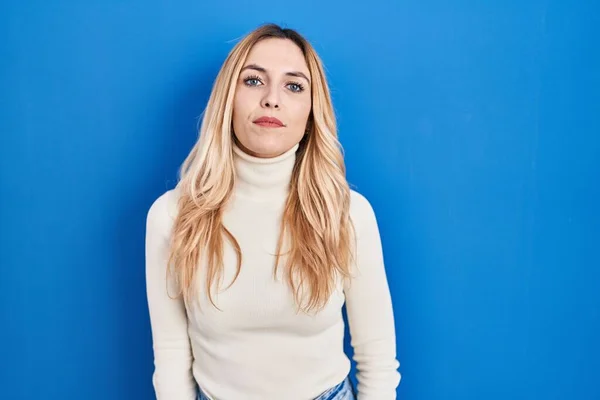 Young caucasian woman standing over blue background relaxed with serious expression on face. simple and natural looking at the camera.