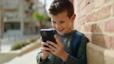 Sarışın çocuk sokakta akıllı telefon kullanıyor.