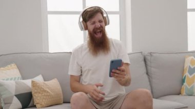 Genç kızıl adam evde müzik dinliyor ve dans ediyor.