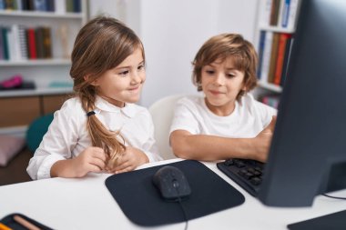 Erkek ve kız kardeş öğrenciler sınıfta masada otururken bilgisayar kullanıyorlar.