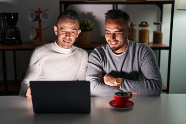 Bilgisayar laptopu kullanan eşcinsel çift kameraya seksi bir ifadeyle bakıyor, neşeli ve mutlu bir yüzle.. 