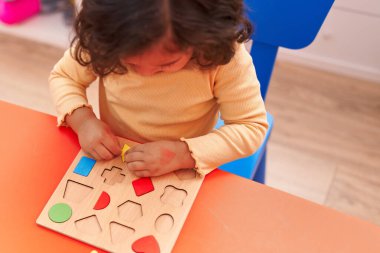 Anaokulunda masada oturmuş matematik bilmecesiyle oynayan sevimli İspanyol çocuk.